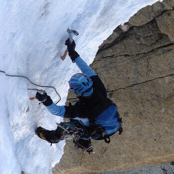 Alpiniste équipé de piolets et crampons, encordé avec un baudrier, évoluant sur la paroi de la montagne enneigée, avec son sac à dos