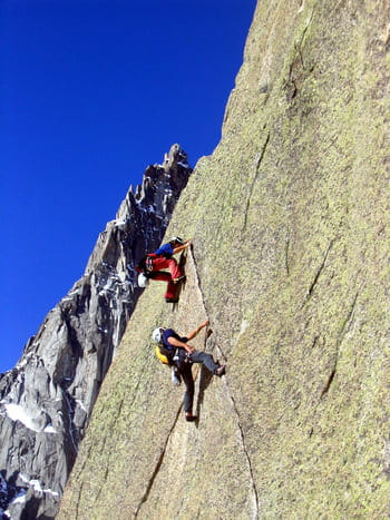 Deux grimpeurs escaladant une paroi de granit en utilisant une fissure comme prise principale en Catalogne.