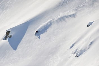 Skieur en action, effectuant une descente freeride dynamique dans la poudreuse.