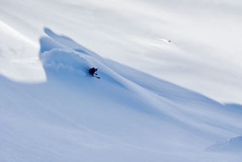 Skieur seul glissant au milieu de neige fraîche, sans rocher à l'horizon, sous l'ombre imposante de la montagne.