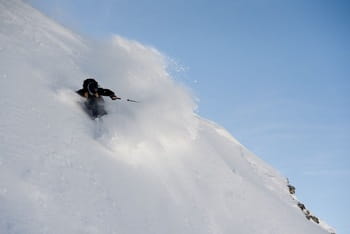 Skieur en pleine descente, effectuant un virage dans de la poudreuse profonde.