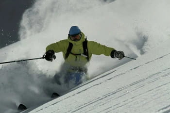 Freerideur effectuant une descente dynamique dans de la poudreuse, soulevant un nuage de neige tel une poussière scintillante lors d'un virage serré