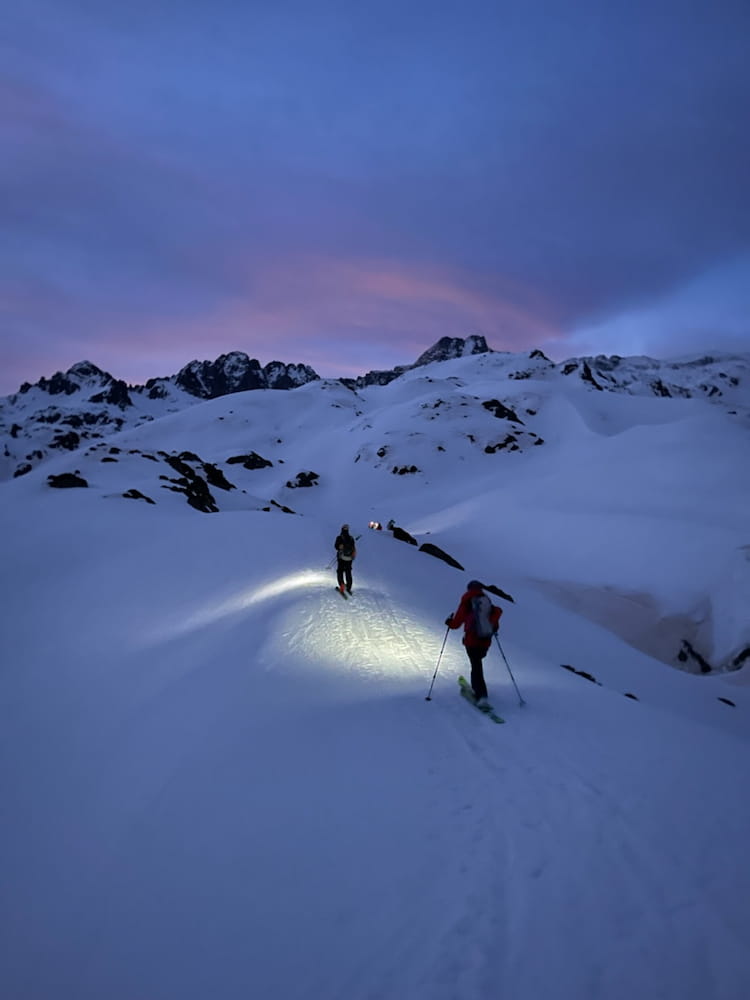 Deux skieurs en ski de randonnée rentrant au crépuscule, éclairés par des lampes frontales, sous un ciel aux teintes rosées et bleues sur les hauteur de Puyvalador. Des sorties ski de rando / alpinisme accompagné d'un guide de haute montagne sans les Pyrénées au départ de Cerdagne / Capcir depuis font-romeu, les Angles, Formiguères, Porté Puymorens, Cambre d’aze ...