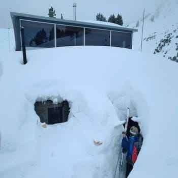 Un skieur rentrant dans un refuge complètement recouvert de neige pour y passer la nuit pendant son raid à ski accompagné par un guide de haute montagne. Une excursions en ski et alpinisme personnalisée dans les Pyrénées, au départ de l'Andorre, l'Espagne et la France à la découverte des Encantats, l'Aneto, le Val d'aran et le Queyras.