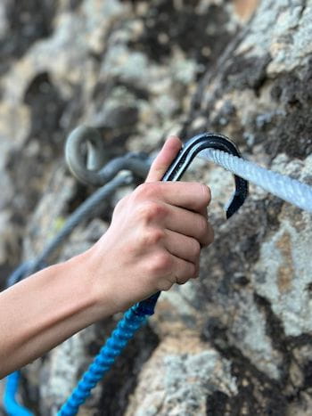 Main accrochant le mousqueton au câble de la via ferrata avec guide de Sensations Pyrénées près de Font-Romeu