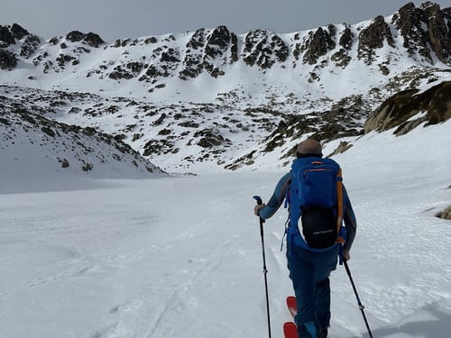 Randonneur à ski lors d'un raid en Andorre, partant de Grandvalira-Grau Roig, encadré par un guide de haute montagne, longeant un lac gelé dans les Pyrénées andorranes, face à d'imposants sommets enneigés.