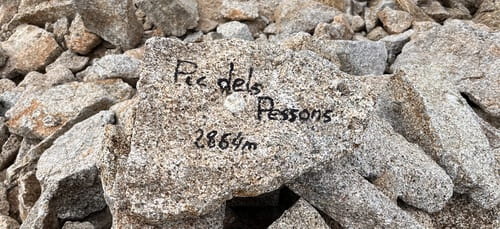 Inscription 'Pic dels Pessons 2 864 m' sur un caillou au sommet, entourée de pierres, marquant le sommet découvert par des skieurs de randonnée lors de leur raid à ski en Andorre, près de Grandvalira-Grau Roig.