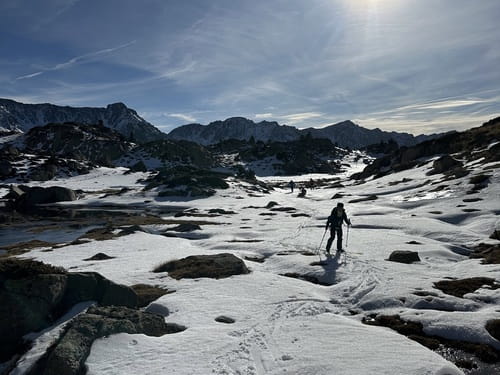 Une personne en ski de randonnée contournant des lacs gelés dans les Pyrénées andorranes, guidés par un professionnel de haute montagne, sur un plateau enneigé entouré de sommets majestueux, lors d'un raid à ski en Andorre.