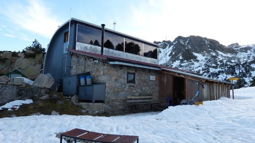 Refuge de Saboredo dans les Encantats, Espagne, devant un tapis de neige avec un sommet au loin, accueillant des skieurs de randonnée encadrés par un guide de Sensations Pyrénées, lors d'un raid à ski dans le cadre enchanteur du Val d'Aran.