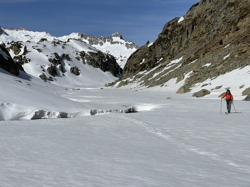 Dans les Encantats, Parc National d'Aigüestortes i Estany de Sant Maurici, un skieur de randonnée guidé par Sensations Pyrénées évolue sur un terrain plat parmi les cimes enneigées, près d'une crevasse révélant un ruisseau s'écoulant sous la neige.