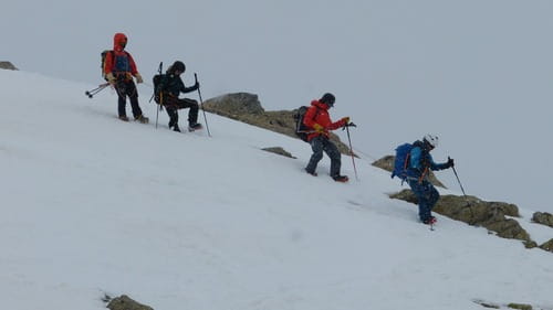 Trois alpinistes en baudriers, casques et crampons, encordés à leur guide de haute montagne, redescendent un sommet dans les Encantats, Parc National d'Aigüestortes i Estany de Sant Maurici, sous un ciel couvert et neigeux.