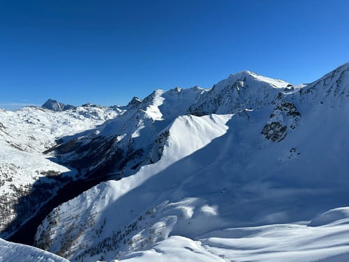 Paysage époustouflant de sommets enneigés sous un ciel bleu immaculé dans le Parc Naturel du Queyras, une véritable invitation à l'exploration et à la découverte de la nature alpine lors d'un raid à ski encadré par un guide de haute montagne de Sensations Pyrénées