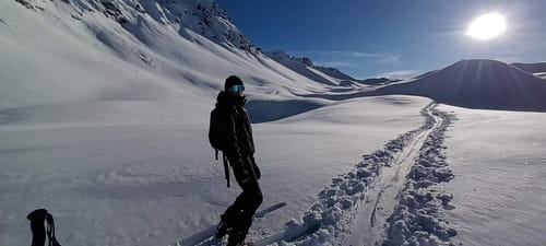 Skieur posant au milieu d'un paysage enneigé éblouissant sous un soleil radieux et un ciel bleu dans le Parc Naturel du Queyras lors d'un raid à ski de randonnée avec Sensations Pyrénées, mettant en évidence la fraîcheur et l'abondance de la neige, marquée par une trace élégante de passage.
