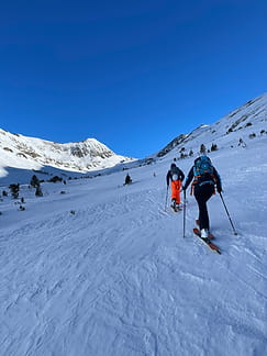 Deux skieurs de randonnée progressant vers le sommet de Tossa Rodona à 2601 mètres, entourés de petits sapins sur la neige.