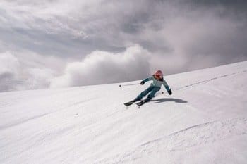 Skieur effectuant une descente hors-piste dans la neige, avec un ciel parsemé de beaux nuages blancs et gris Skieur effectuant une descente hors-piste dans la neige, avec un ciel parsemé de beaux nuages blancs et gris